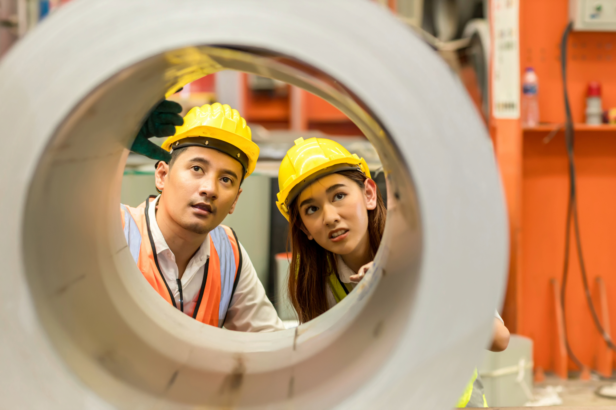 Two construction workers looking through a tube.